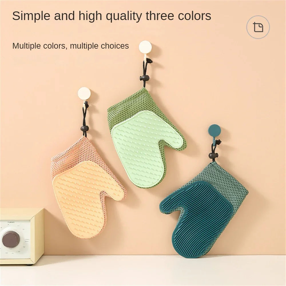 Three silicone pet grooming gloves in yellow, green, and teal hanging on wall hooks.